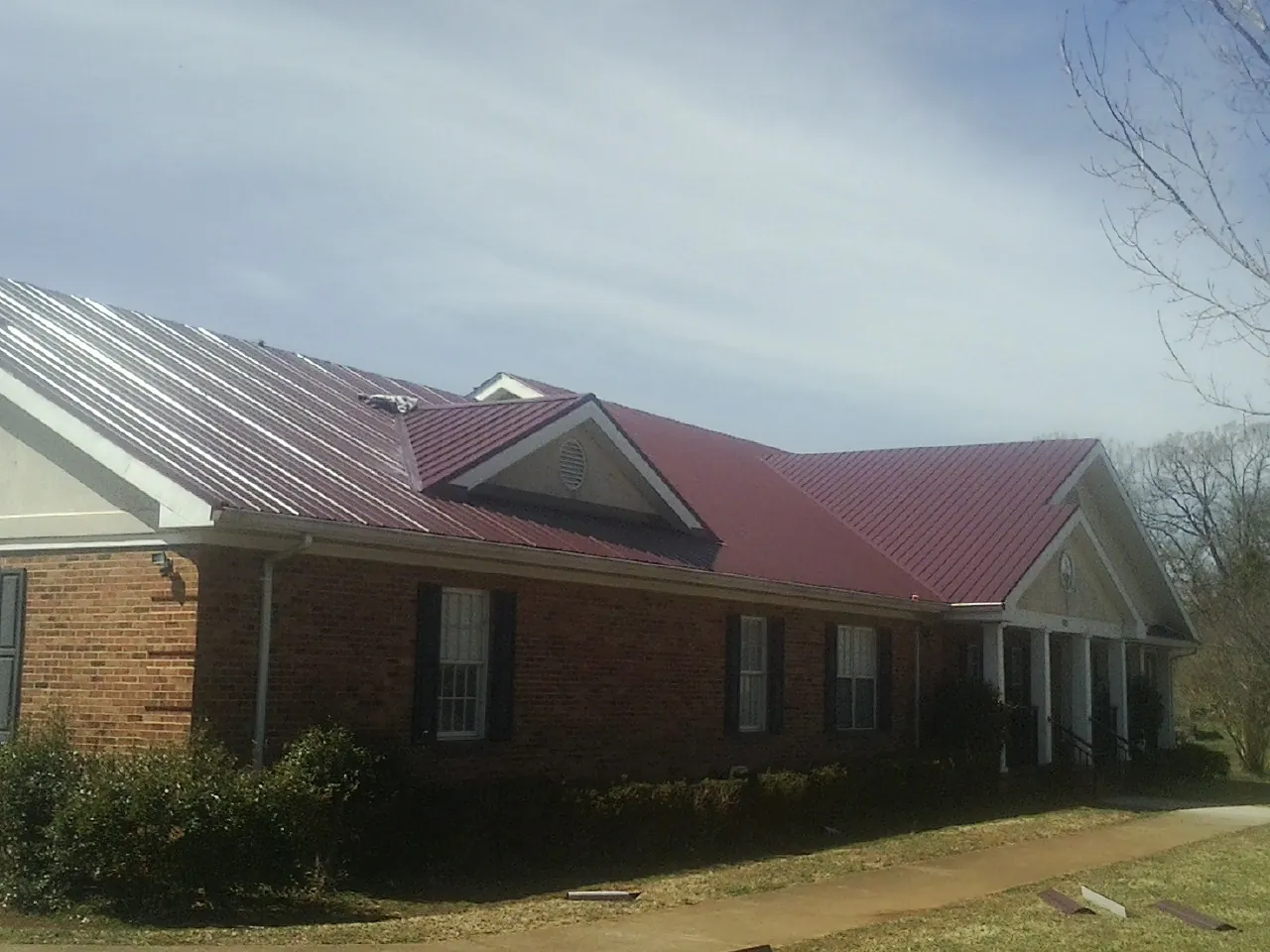Red metal roof with gabled entries on a long brick building, from a Hail Damage Roof Repair job in Atkinson